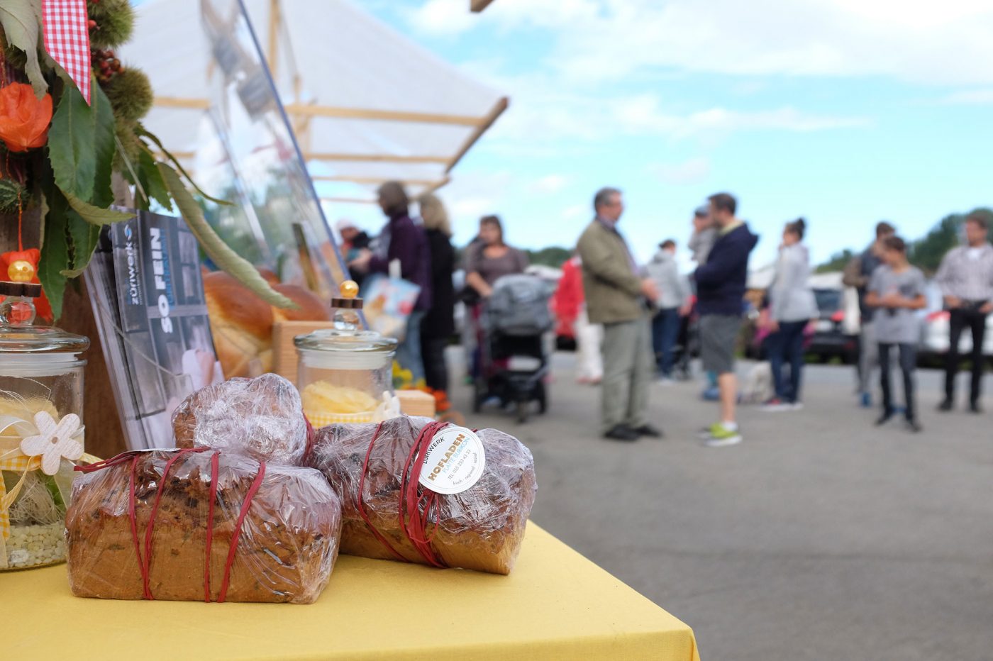 Feines frisches Brot liegt auf einem Marktstand. Im Hintergrund stehen Besucher am Degustations-Stand schlange.