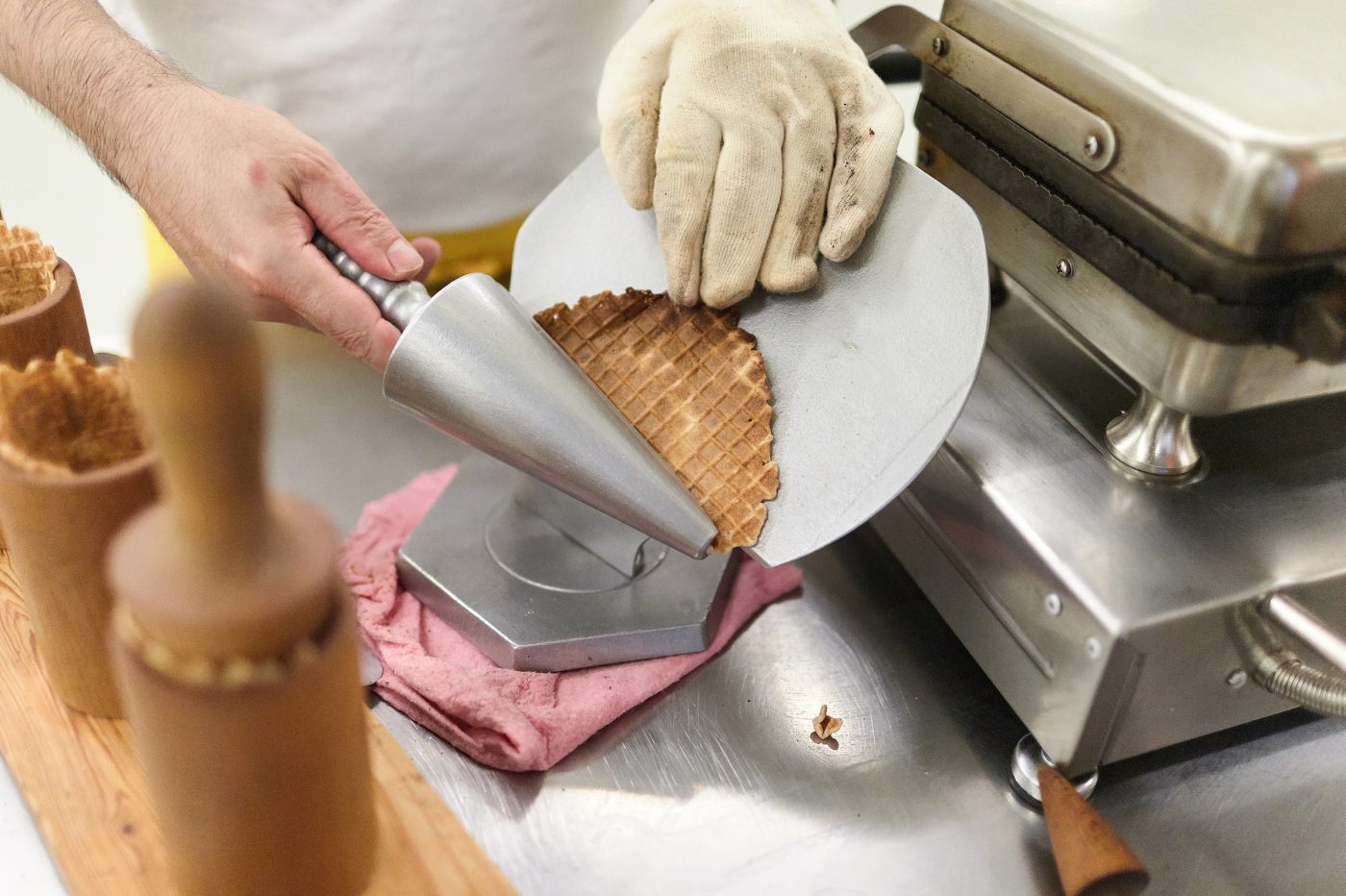 Ein frisch gebackene Waffel wird mit einem silbernen Cornet Rollwerkzeug zubereitet.