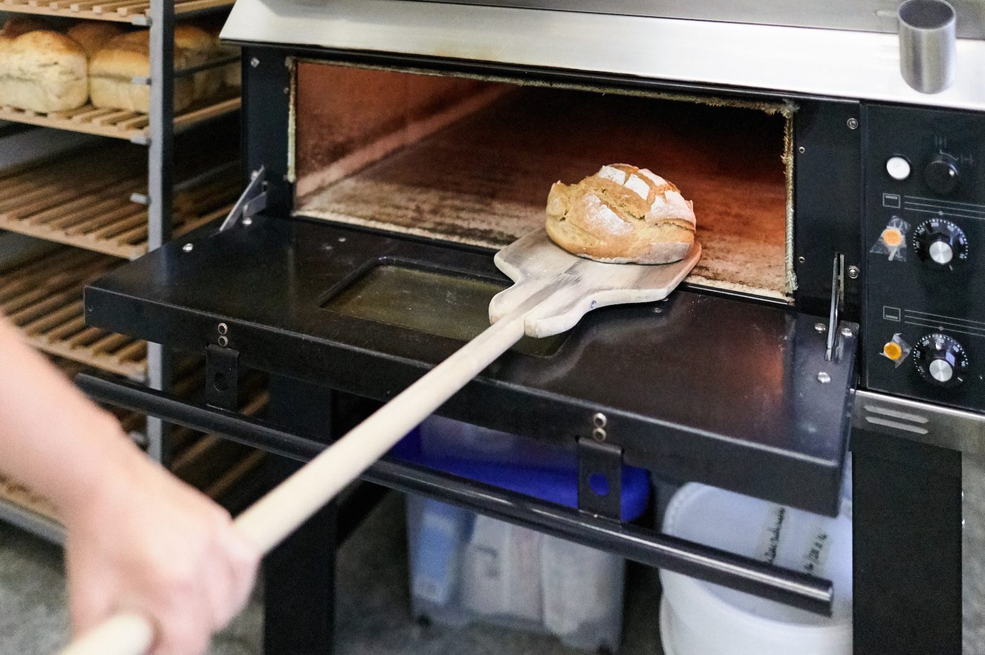 Eine Hand nimmt das auf der hölzernen Brotkelle liegende Brot aus dem Industriebackofen raus