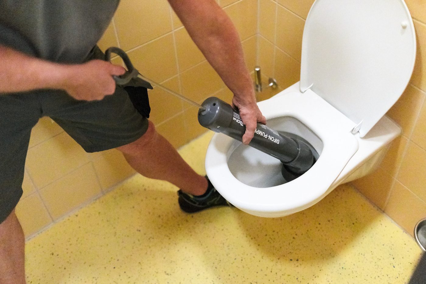 Eine Person steckt das graue Entstopfungswerkzeug in eine Toilette