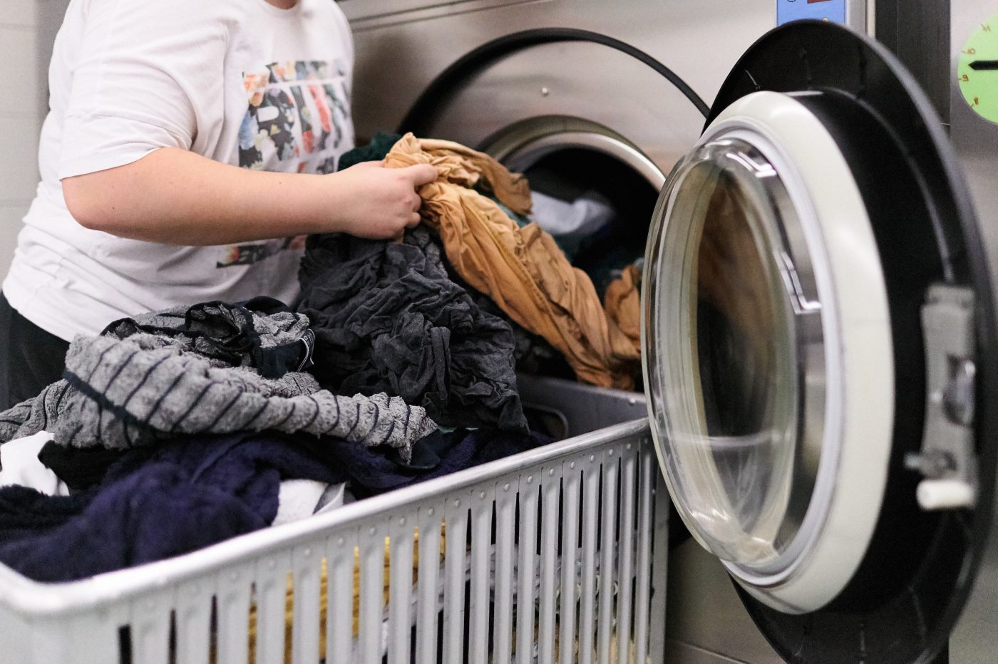 Frisch gewaschene Kleider werden aus der grossen Industriewaschmaschine gerade in den davorstehenden Wäschewagen gehoben